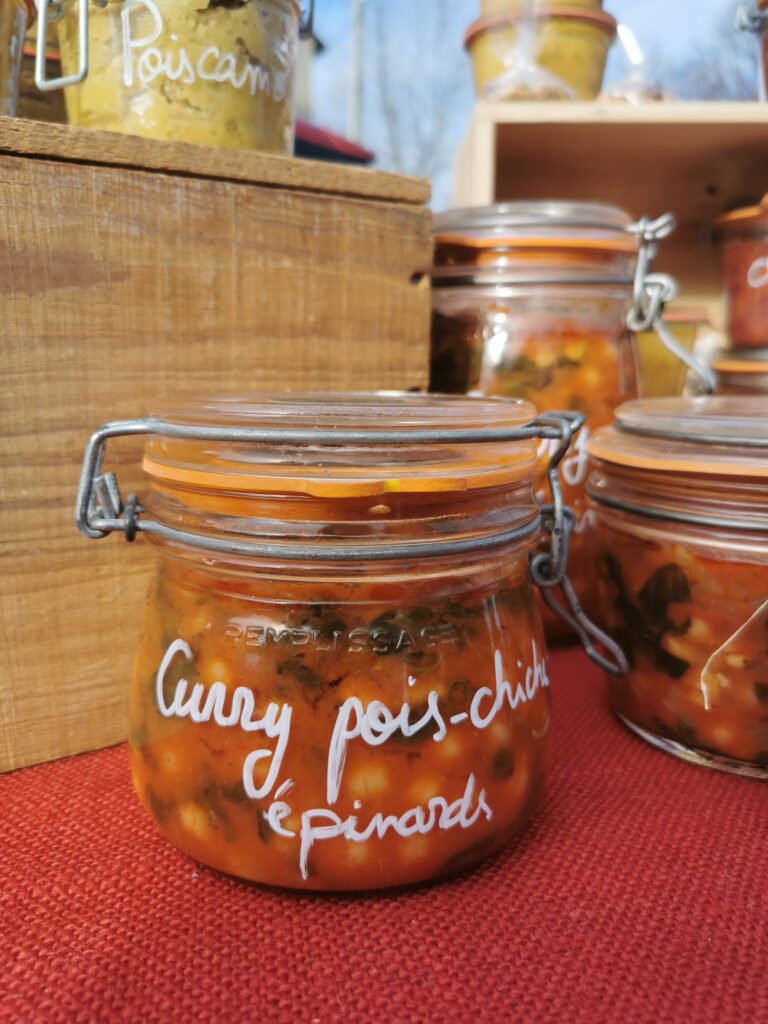 Bocal en verre contenant un curry de pois chiches et épinards fait maison, exposé sur un stand de marché zéro déchet.